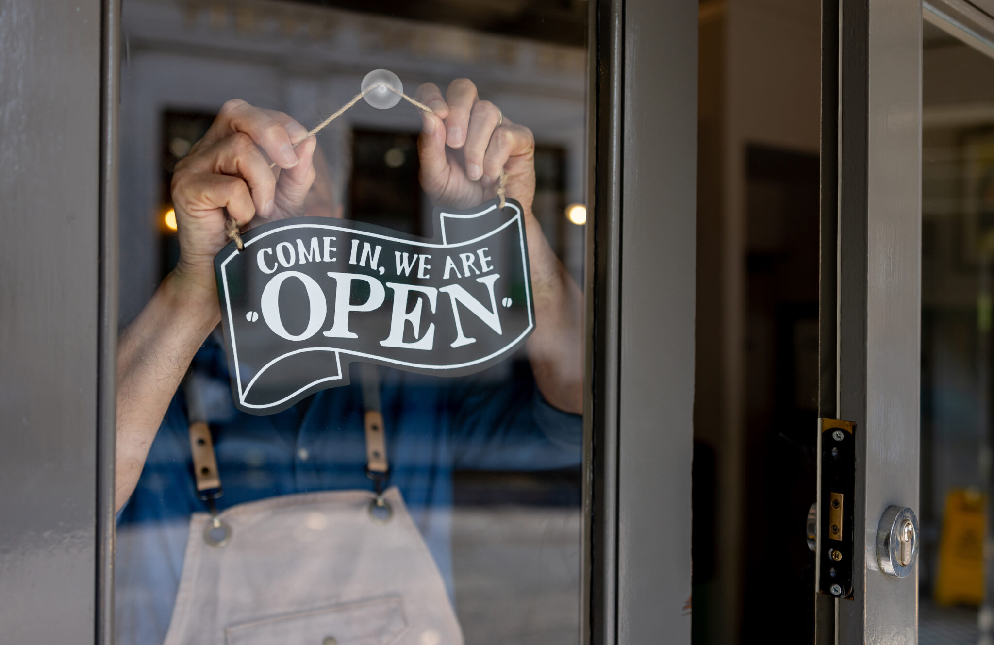 Close-up on a business owner hanging an open sign on the door of his restaurant - food and drink establishment concepts